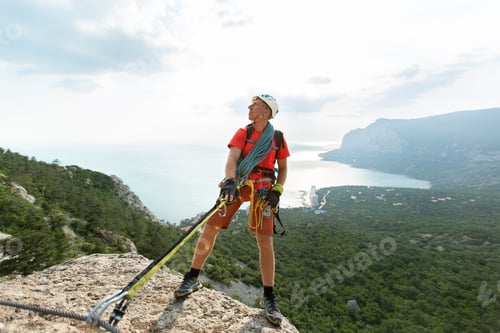 Preview: Climber climbs the mountain on a cable with a view of the forest and the sea.