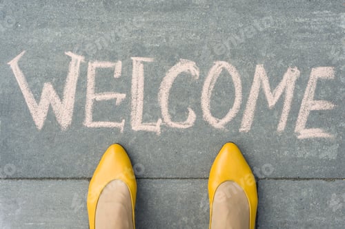 Preview: Female feet with text welcome written on grey sidewalk