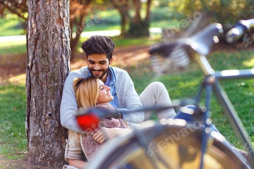 Preview: Couple in love sitting in a autumn park leaning against a tree embracing one another.