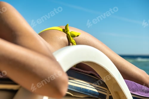 Preview: Close up of young woman hip and shoulder laying on beach chair at sea shore sunbathing.