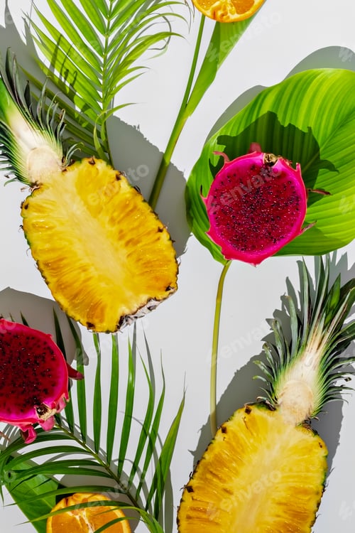 Preview: Sliced pineapple, dragon fruit, and orange arranged with green tropical leaves on white background.