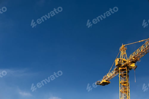 Preview: Construction crane tower in sun light beams on background of blue sky
