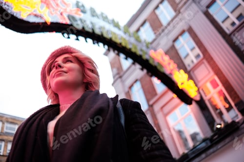 Preview: Young woman illuminated by red neon light in London street.