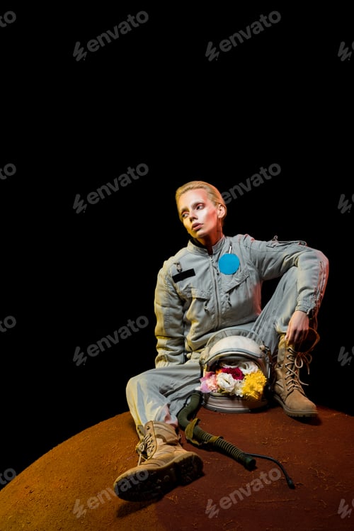 Preview: beautiful astronaut in spacesuit with flowers in helmet sitting on planet