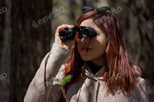 Preview: Young woman looking through binocular outdoor