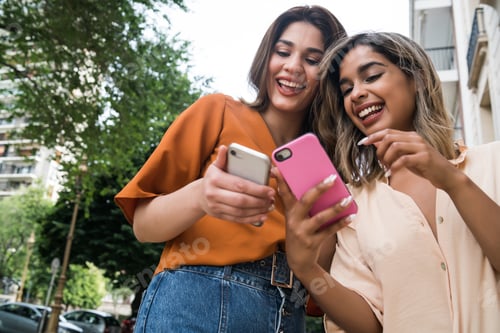 Preview: Two friends using mobile phone outdoors.