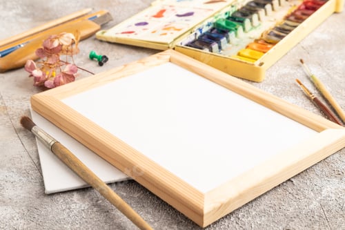 Preview: Drawing accessories set: brushes, pencils, watercolor, frame on brown concrete. Side view