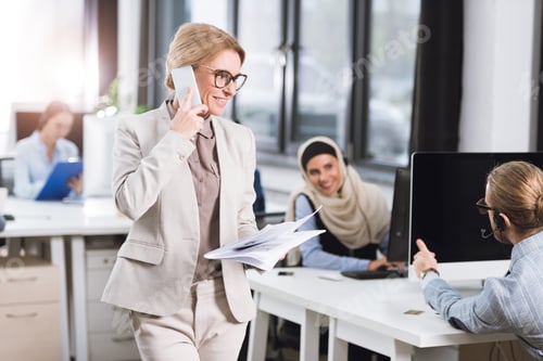 Preview: selective focus of smiling businesswoman with newspaper in hand talking on smartphone in office