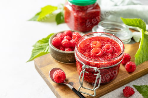 Preview: Delicious raspberries jam or jelly and fresh raspberries on a stone table.