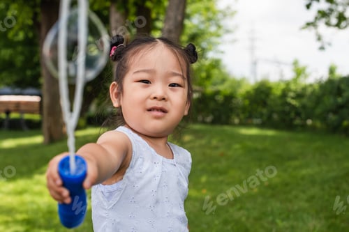 Preview: asian girl in dress holding blurred bubble stick near soap bubble outside