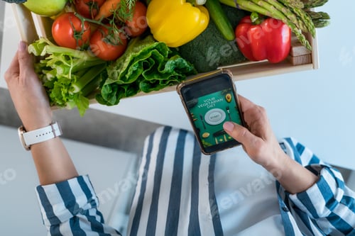 Preview: Woman holding a box with fresh organic vegetables and phone with vegetarian diet program app