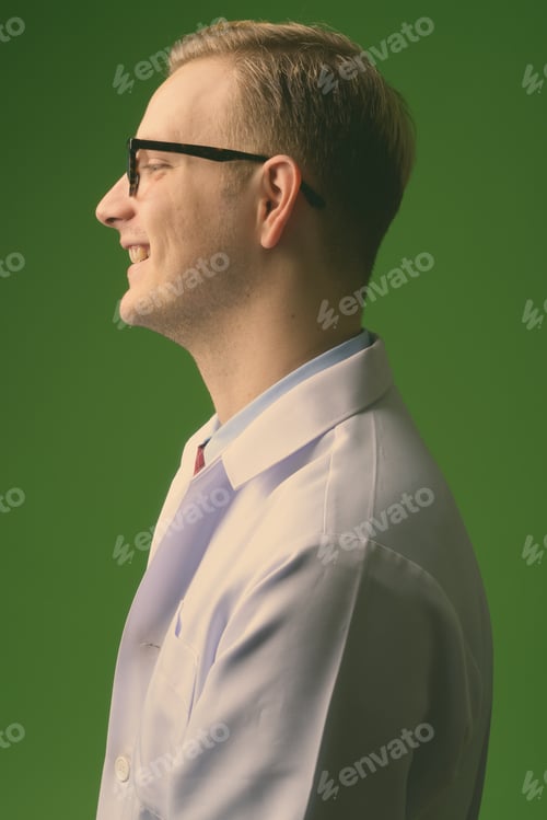 Preview: Young handsome man doctor with blond hair against green background