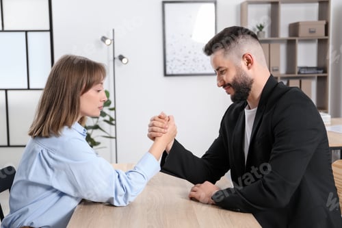 Preview: Businesspeople arm wrestling at wooden table in office