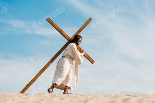 Preview: bearded man walking with wooden cross against sky in desert