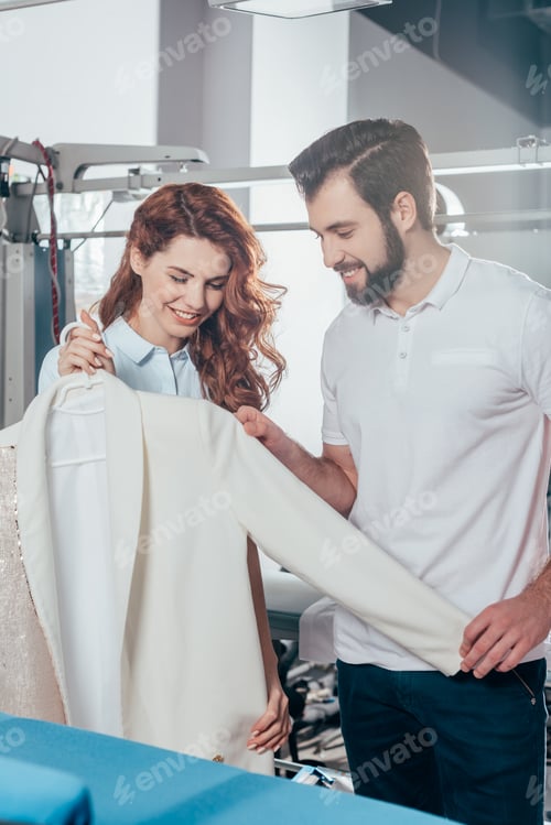 Preview: young dry cleaning workers holding clean white jacket at warehouse
