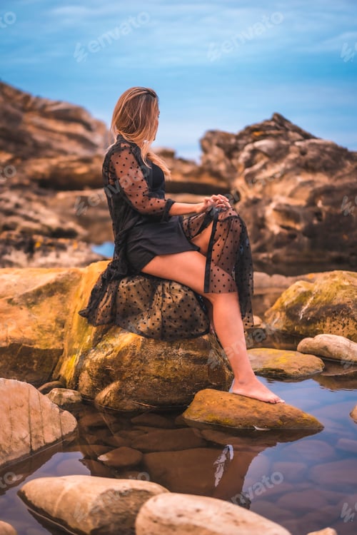 Preview: Young brunette Caucasian woman in a long black transparent dress on some rocks