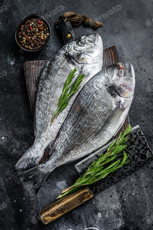 Preview: Raw Sea bream dorado fish on a cutting board. Black background. Top view