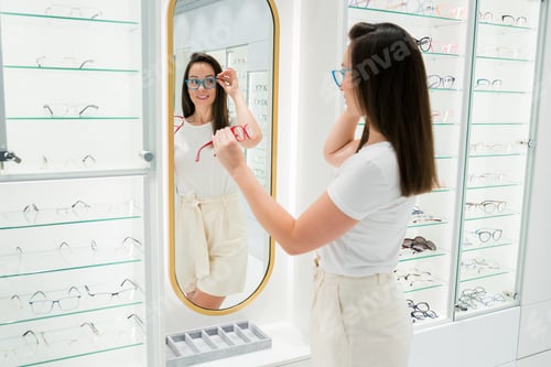 Preview: Smiling female looking in the mirror how different glasses look on her and selecting frames