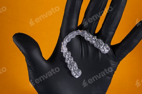 Preview: Doctor hand holding a clear dental aligner with the yellow background