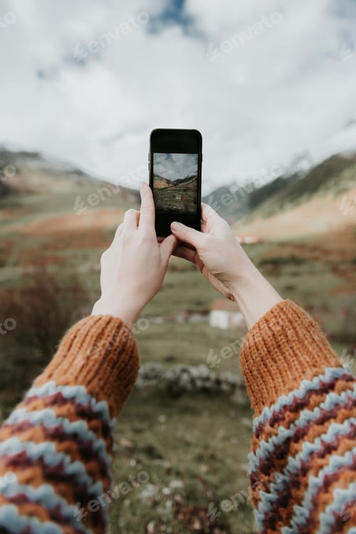 Preview: Woman taking photo on smartphone of valley with high hills in cloudy weather