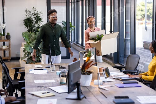 Preview: African American colleagues welcoming new team member with box at modern office