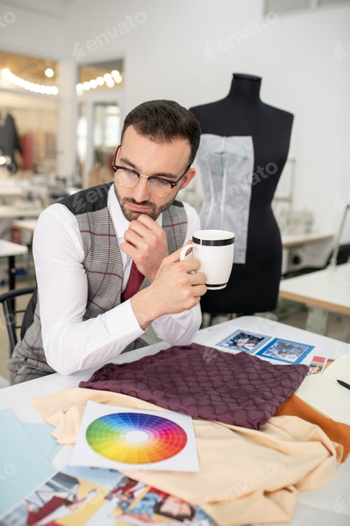 Preview: Male tailor sitting at the table, holding cup