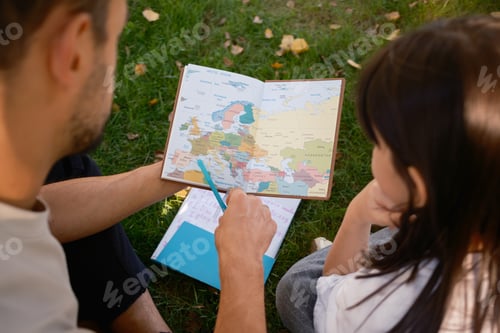 Preview: Father and daughter exploring a world map together in the park
