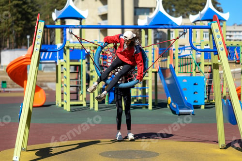 Preview: two teenager girls in caps on the playground. children's swing.