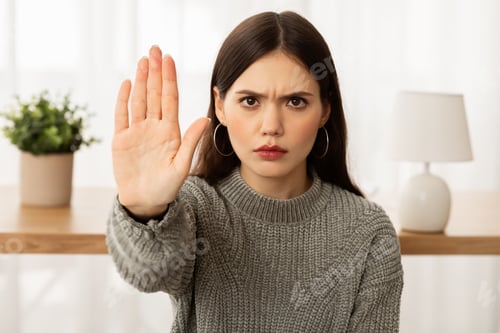 Preview: Angry young brunette woman showing stop gesture at camera