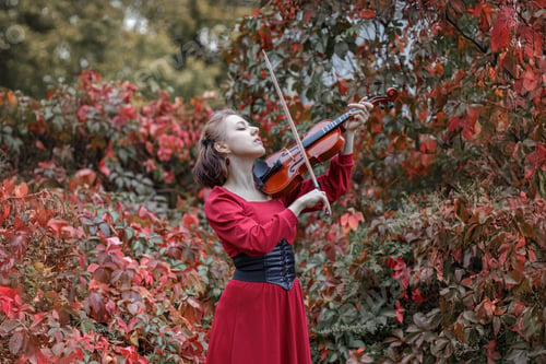 Preview: Young woman in red park playing violin in autumn garden