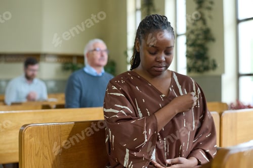 Preview: Young black woman with her eyes closed crossing herself during silent prayer