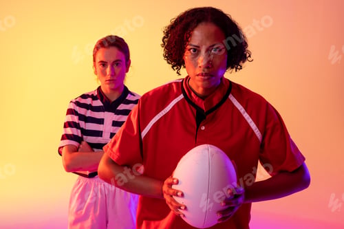 Preview: Portrait of diverse female rugby players with rugby ball over neon pink lighting