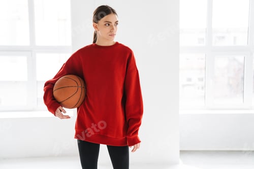 Preview: Athletic young sportswoman working out with basketball indoors