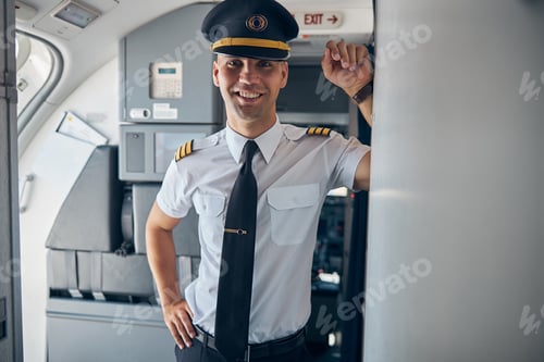 Preview: Cheerful male captain standing inside commercial airplane
