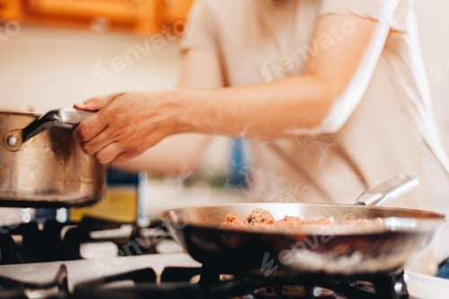 Preview: young millennial woman at home in the kitchen cooking on gas stove