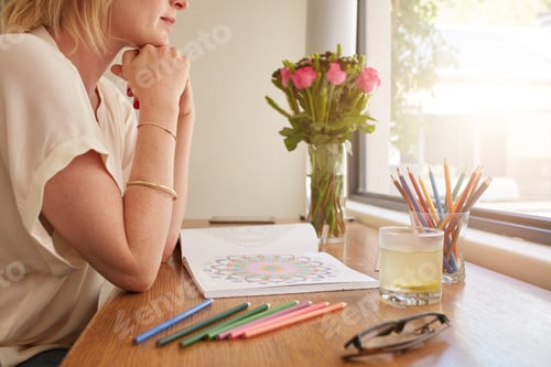 Preview: Woman sitting at a table and thinking with adult coloring book