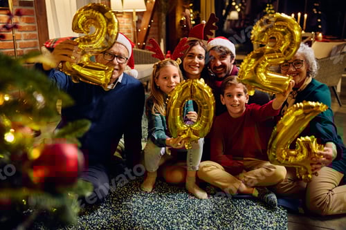 Visualização: Feliz família multigeracional comemorando o Ano Novo enquanto segura balões de 2024 e olha para a câmera.