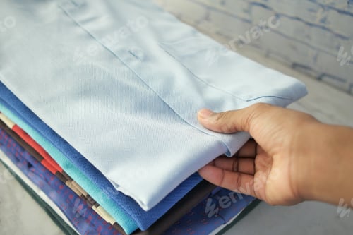 Preview: Stack of Folded Shirts with Hand Holding Top