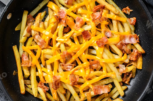 Preview: Golden French fries fried with cheddar cheese and bacon in a pan. Black background. Top view