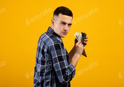 Preview: Young man with wallet full of money being greedy over his wealth on orange studio background
