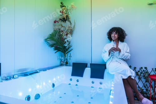 Preview: Beautician relaxing in hydromassage tub holding drink after spa treatment