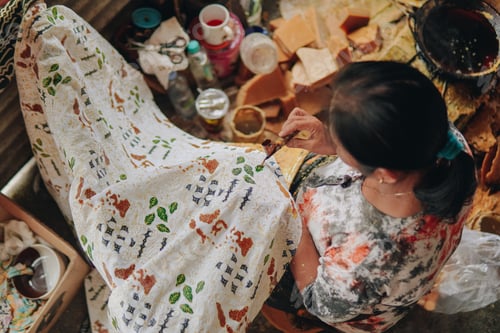 Preview: Top view of a woman drawing the colorful design pattern of Indonesian batik tulis fabric.
