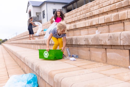 Preview: Multiracial elementary schoolgirls cleaning plastic waste on school building steps