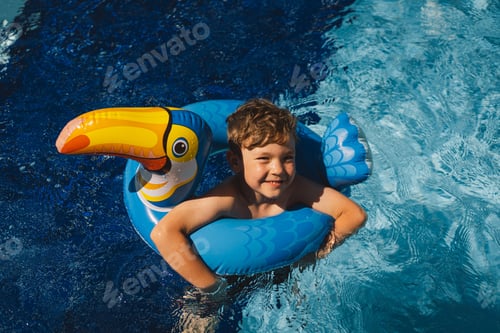 Preview: A boy in a swimming pool on a sunny day, using an swimming circle designed to look like a blue bird.