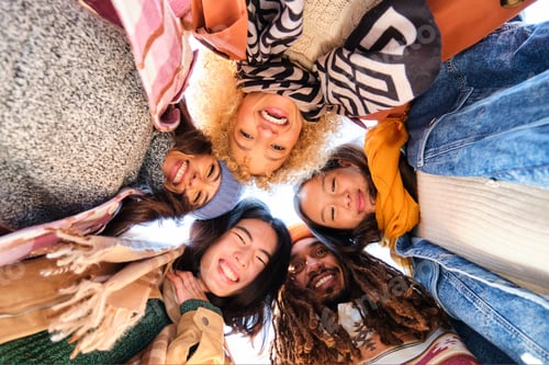 Preview: Low angle view of multiracial group of friends standing in circle and smiling.