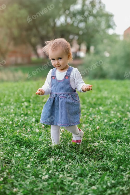 Preview: A little girl walks on the grass with her hands raised and a sly look on her face