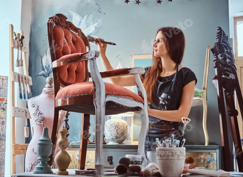 Preview: Female artist painting vintage chair in white color with paintbrush in workshop.