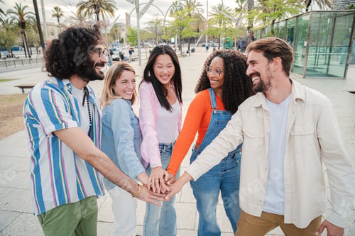 Preview: Meeting of smiling young adult people, men and women stacking hands showing unity or support