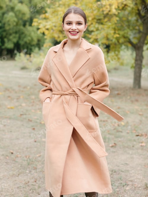 Preview: Woman with brown hair in a long trench coat walking on the park.