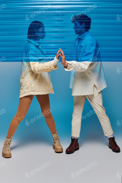 Preview: full length of trendy interracial couple touching hands of each other behind blue plastic sheet